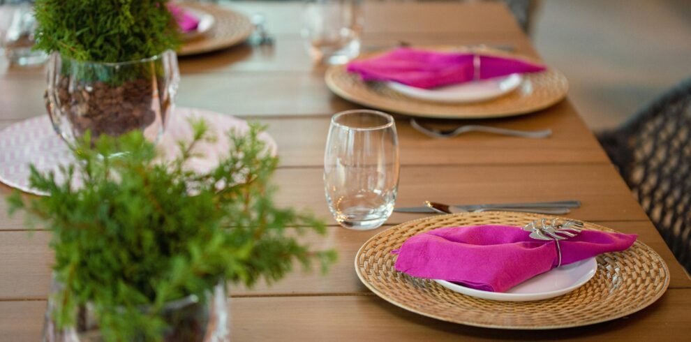 A beautifully arranged dining table with pink napkins and plant centerpieces, perfect for a stylish event.